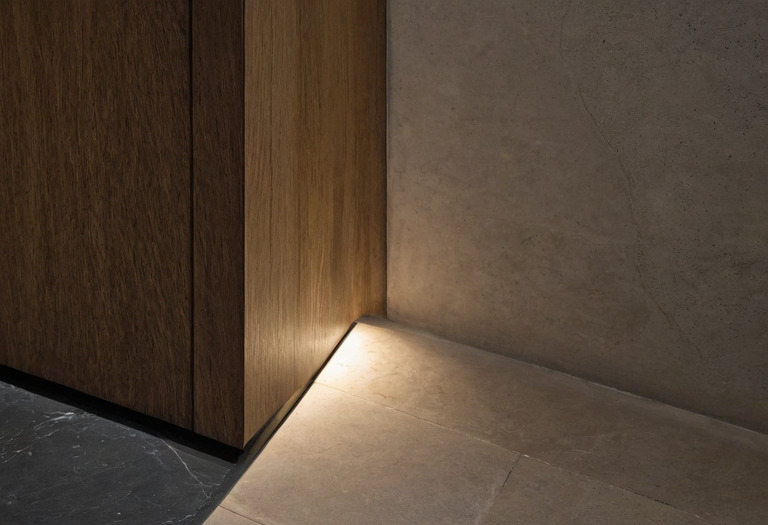 Recessed dark shadow gap running along a plaster wall above a stone floor