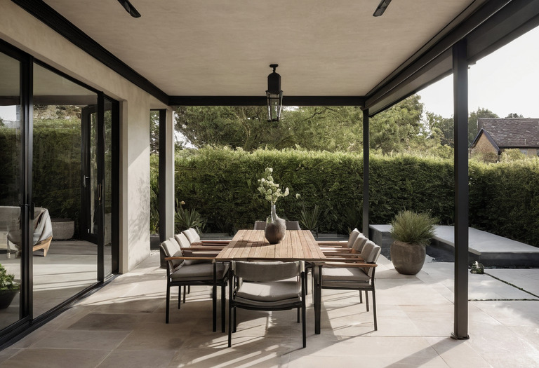 Covered outdoor dining and seating area with stone paving and a drained threshold