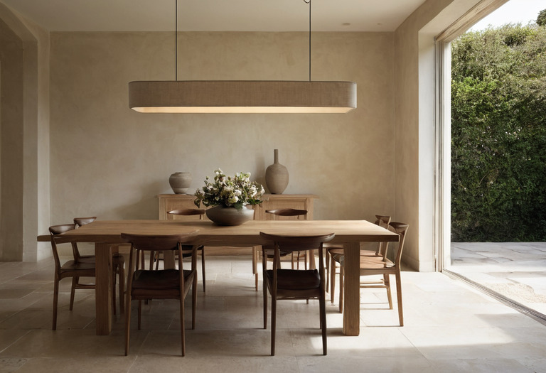 Shielded pendant centered above a long timber dining table in a measured interior